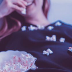 Woman with TV remote eating popcorn